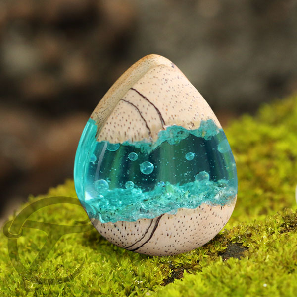 The base for this Epoxy ear plug is a teardrop shaped wood plug hand carved from light tamarind wood. We then crack the plug into two pieces and fill the space in-between the wood plug with a aqua coloured epoxy jewelry resin with some bubbles added to ex